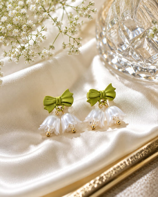 Close view of green bow studs with white pearl bell flowers and gold bead tips