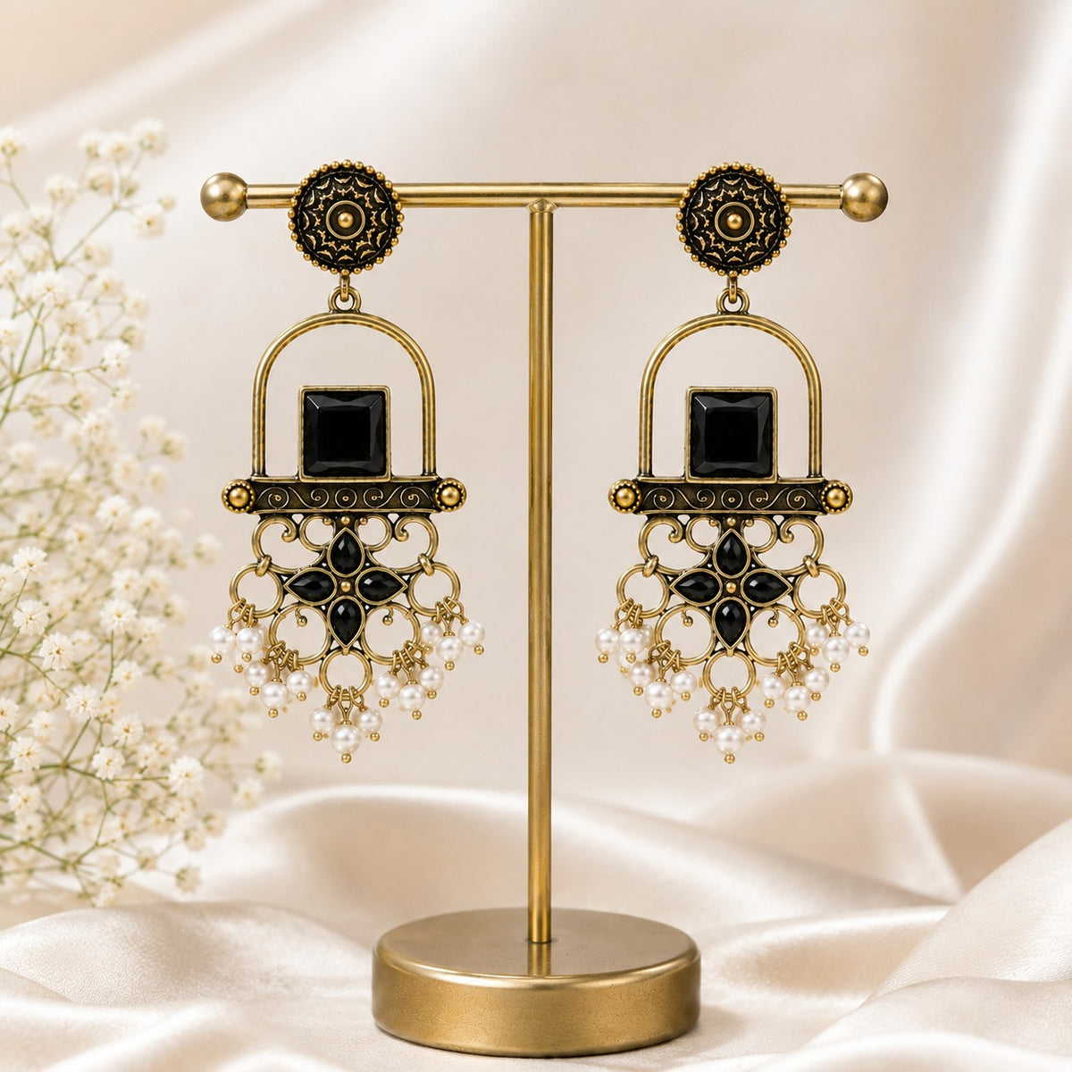 Antique gold arch drop earrings with a jet black square stone, filigree apron and faux pearl clusters on a gold stand