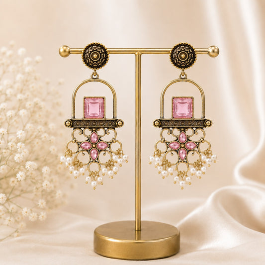 Antique gold arch drop earrings with a rose pink square stone, filigree apron and faux pearl clusters on a gold stand