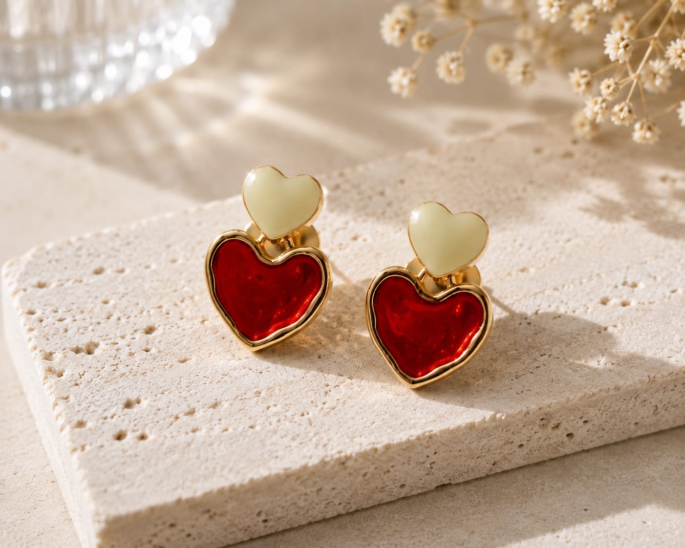 Gold-plated double heart stud earrings in ivory and red enamel on a travertine block