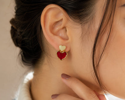 Close view of a model wearing a gold double heart stud earring in ivory and red enamel