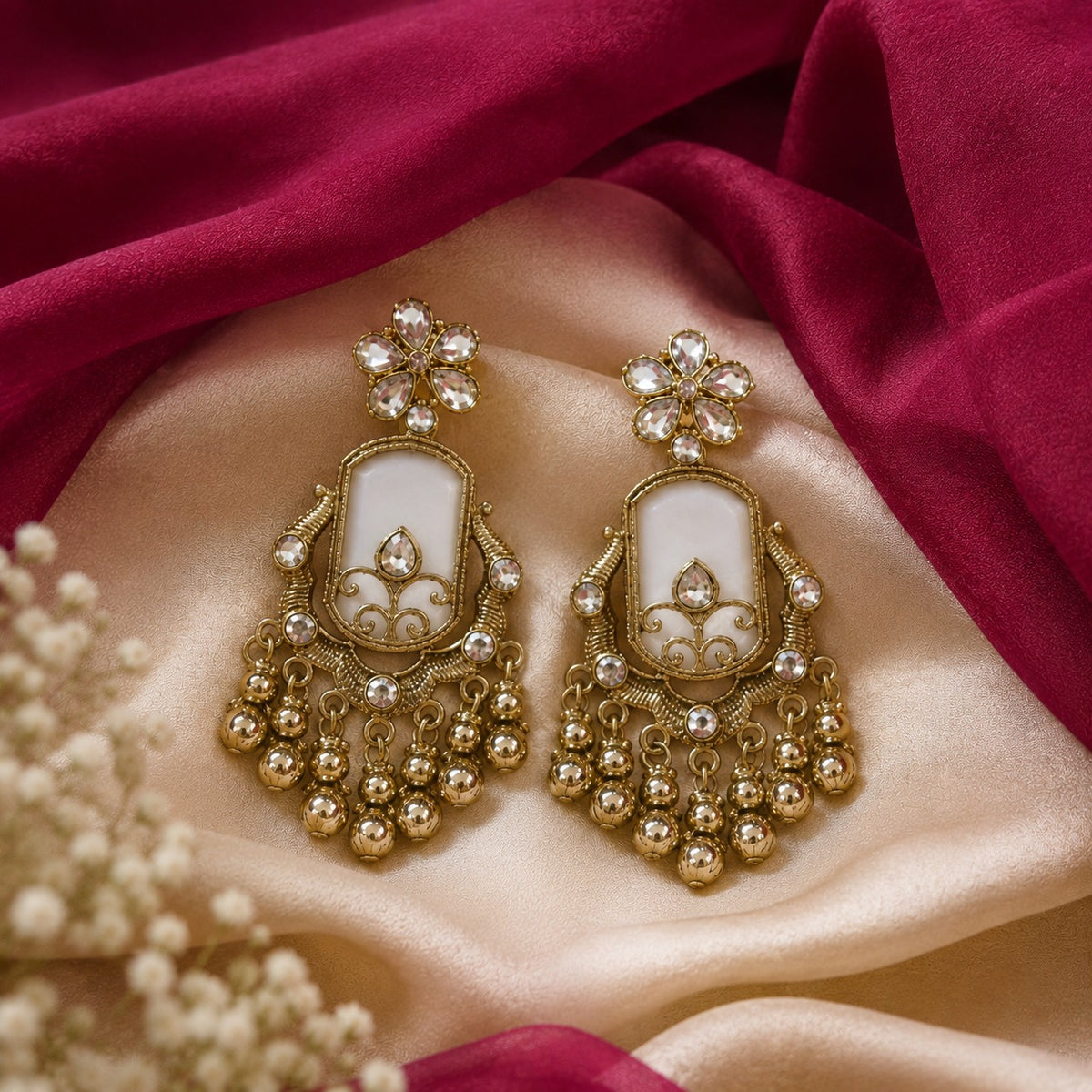 Gold-plated chandbali earrings with an ivory shell panel, crystal flower top and gold ball drops on maroon velvet