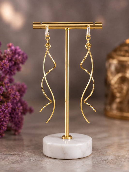 Gold-plated twisted spiral drop earrings with clear baguette crystal studs on a brass display stand