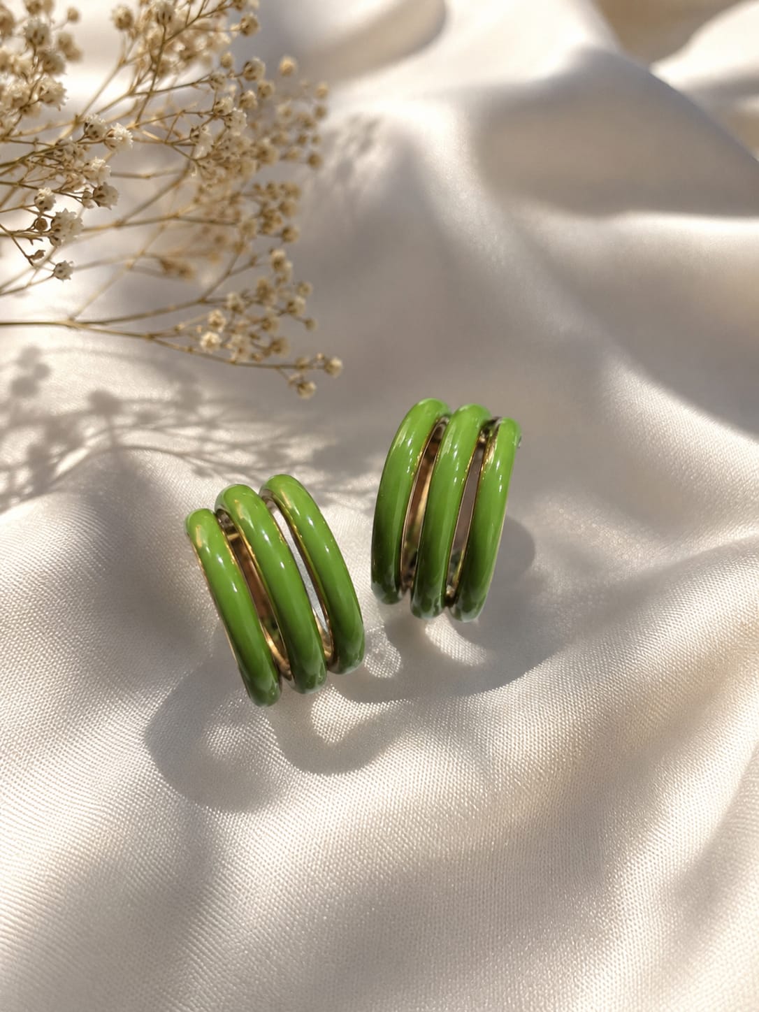 Gold-plated triple-band green enamel hoop earrings on ivory satin with dried gypsophila