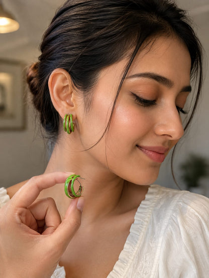 Model in a white top wearing a green enamel triple hoop earring and holding the second hoop