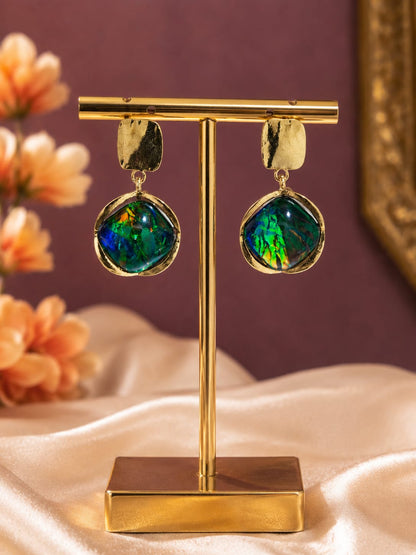 Gold-plated drop earrings with iridescent green and blue glass cabochons on a gold display stand