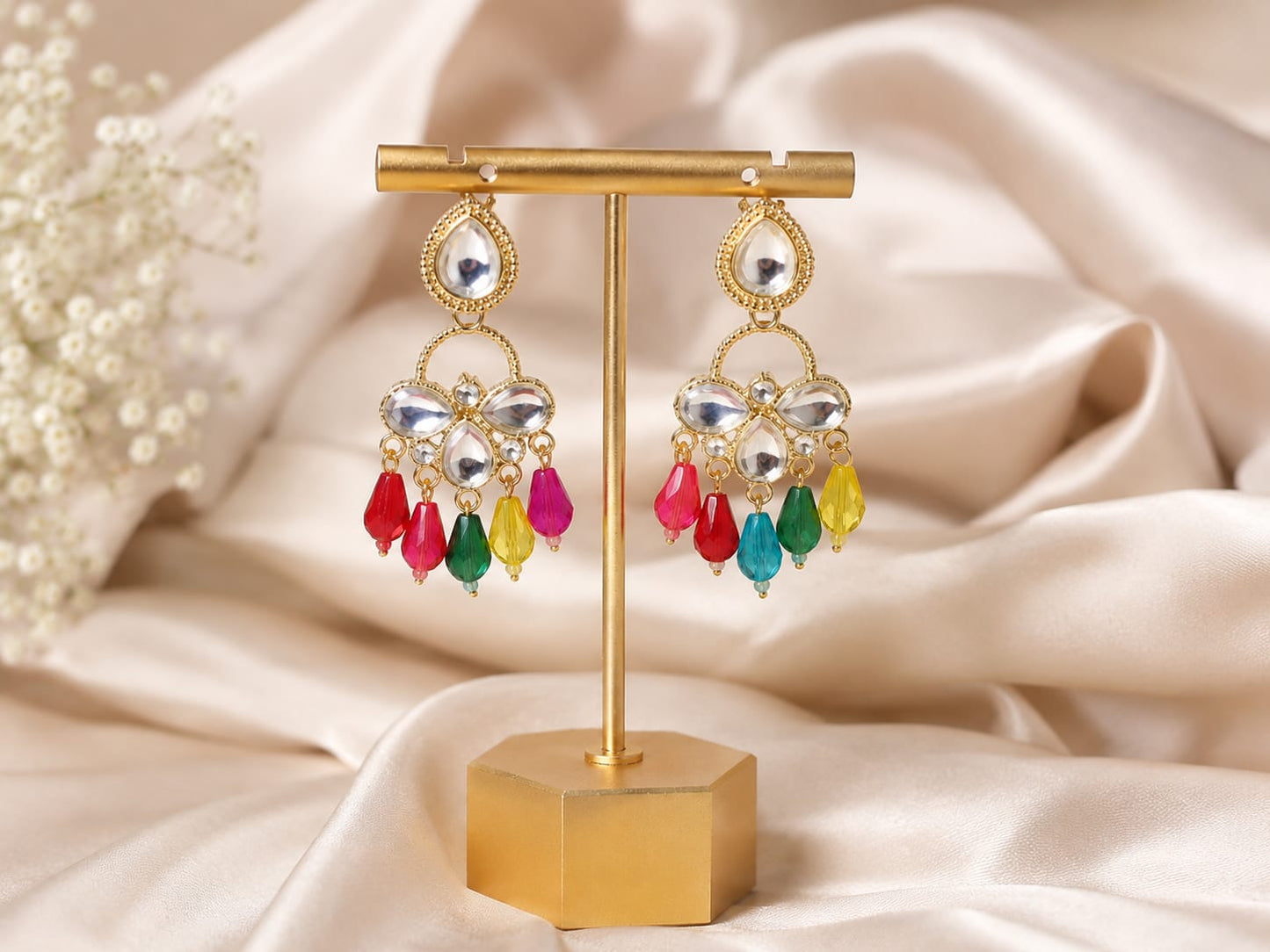 Gold-plated kundan chandelier earrings with multicolour glass bead drops on a gold stand against cream satin