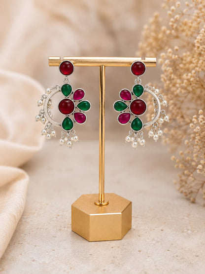 Silver-tone floral chandbali earrings with ruby and emerald glass stones and a pearl fringe on a gold stand