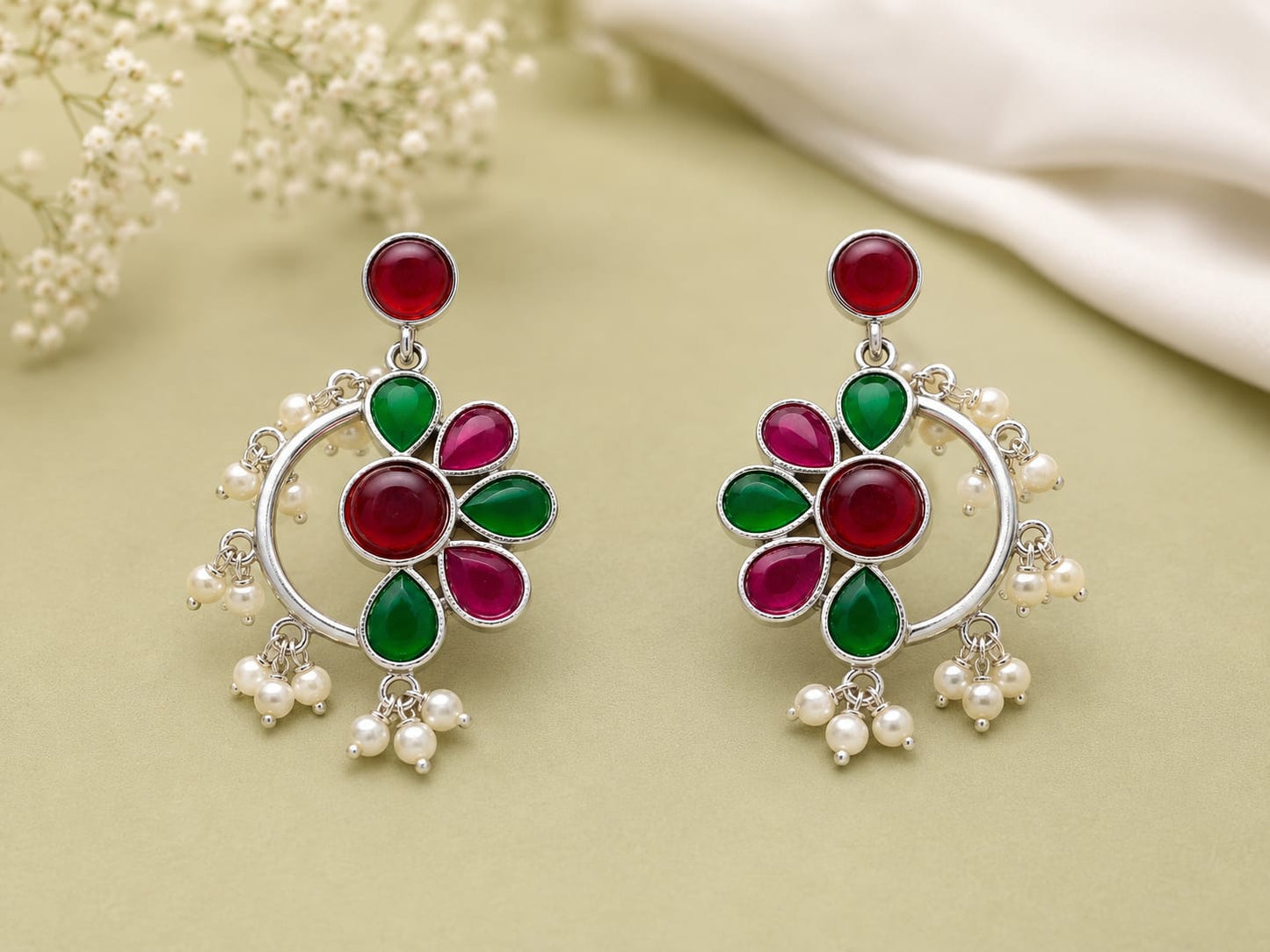Ruby and emerald kundan floral chandbali earrings with pearl clusters on a sage green background