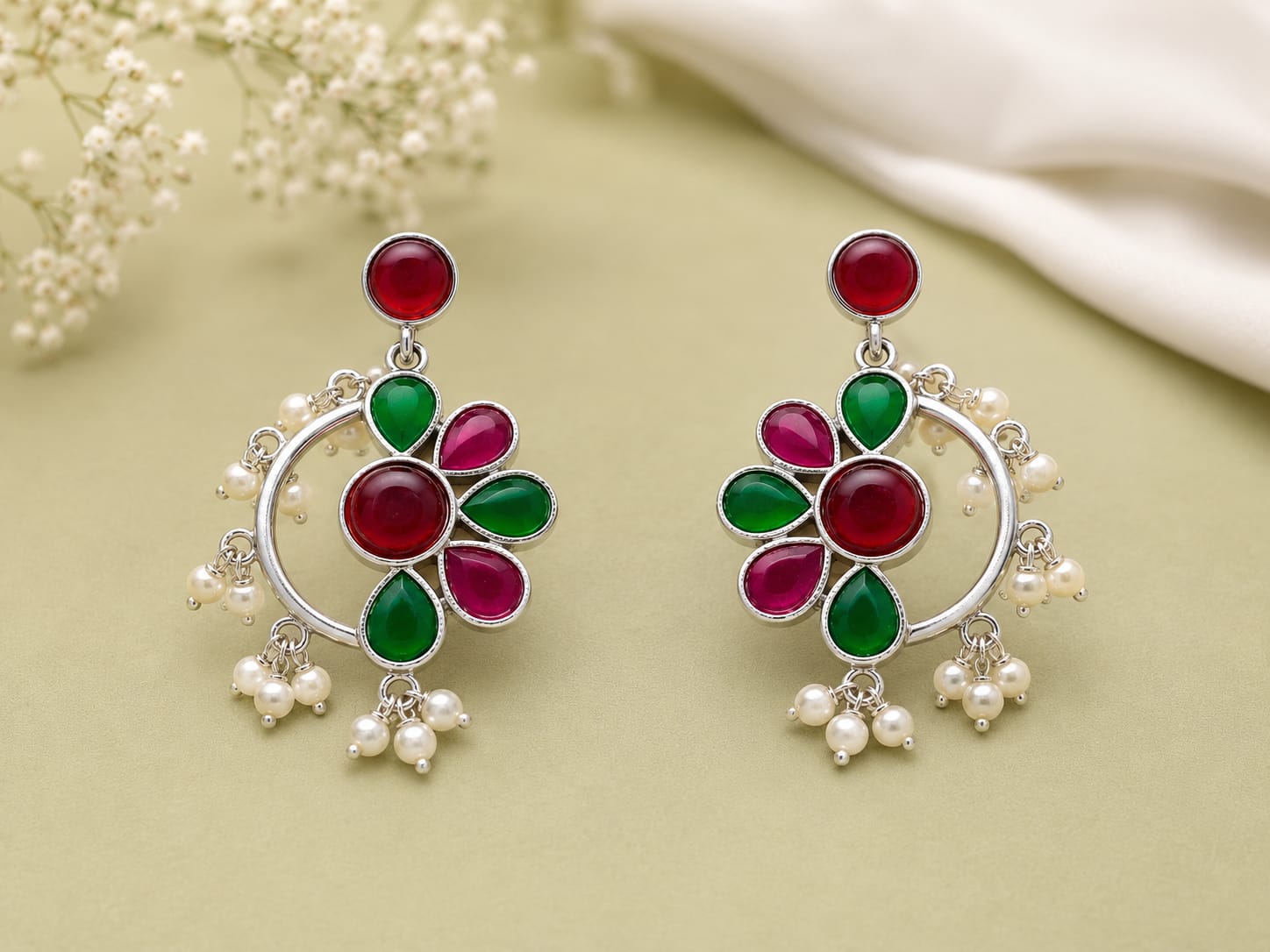 Ruby and emerald kundan floral chandbali earrings with pearl clusters on a sage green background