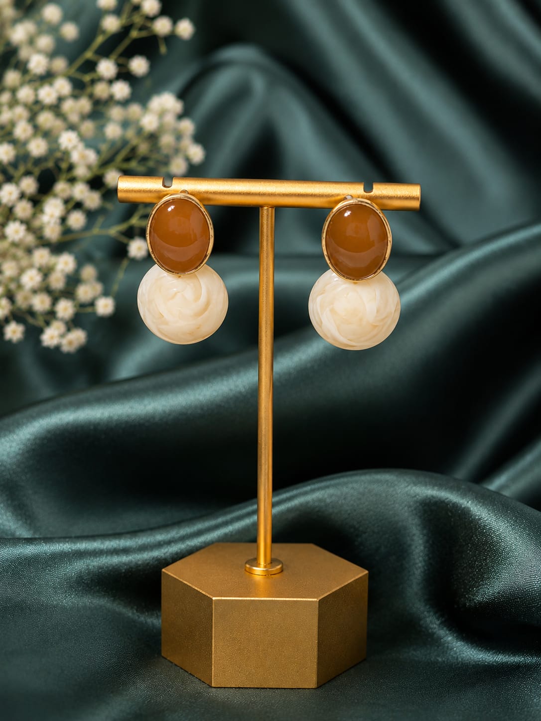 Toffee brown and marbled ivory resin drop earrings on a gold stand against dark green satin