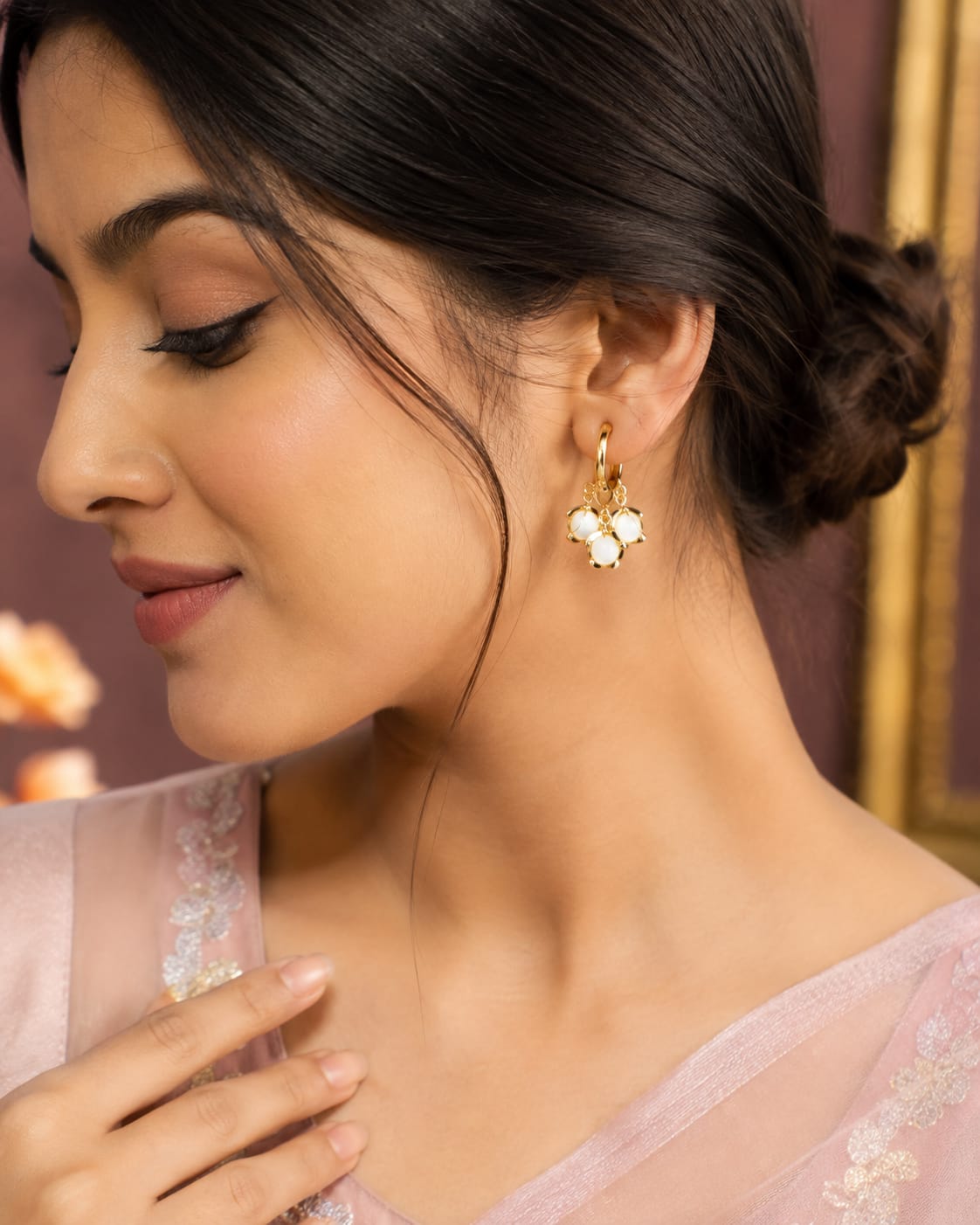 Model in a blush pink saree wearing gold huggie hoops with white stone clusters