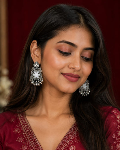 Model in a maroon embroidered kurta wearing oxidised chandbali earrings with a white stone and silver bell fringe