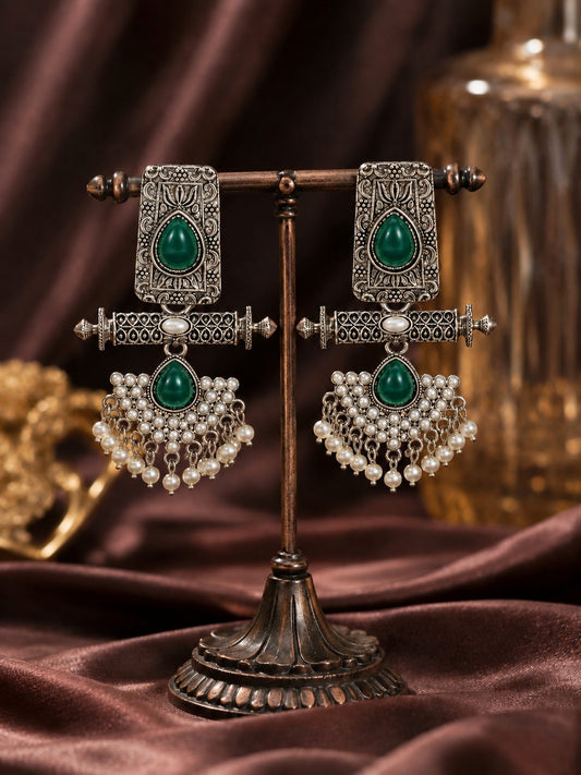 Long oxidised silver earrings with green teardrop stones and a fan of faux pearls on a bronze display stand