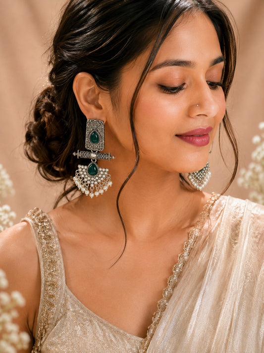 Model in a gold tissue saree wearing long oxidised earrings with green stones and a pearl fan fringe