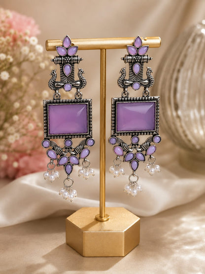 Oxidised silver peacock chandelier earrings with lilac stones and faux pearl clusters on a gold display stand