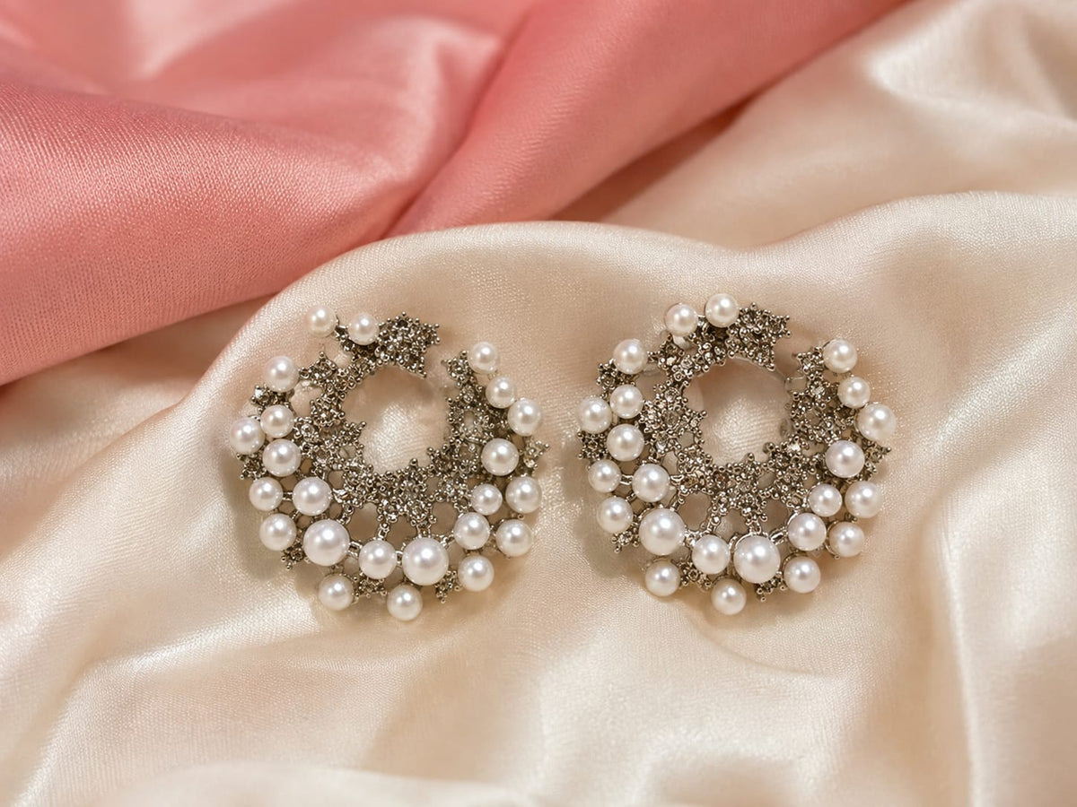 Silver-tone crescent stud earrings in pave crystal filigree edged with graduated faux pearls on ivory satin