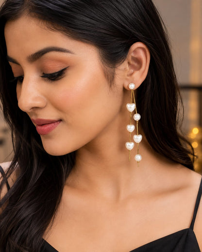 Model in a black top wearing long pearl heart chain drop earrings