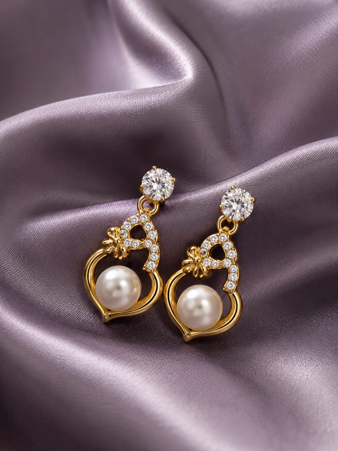Gold-plated heart earrings with a cream pearl centre and crystal accents on lilac satin