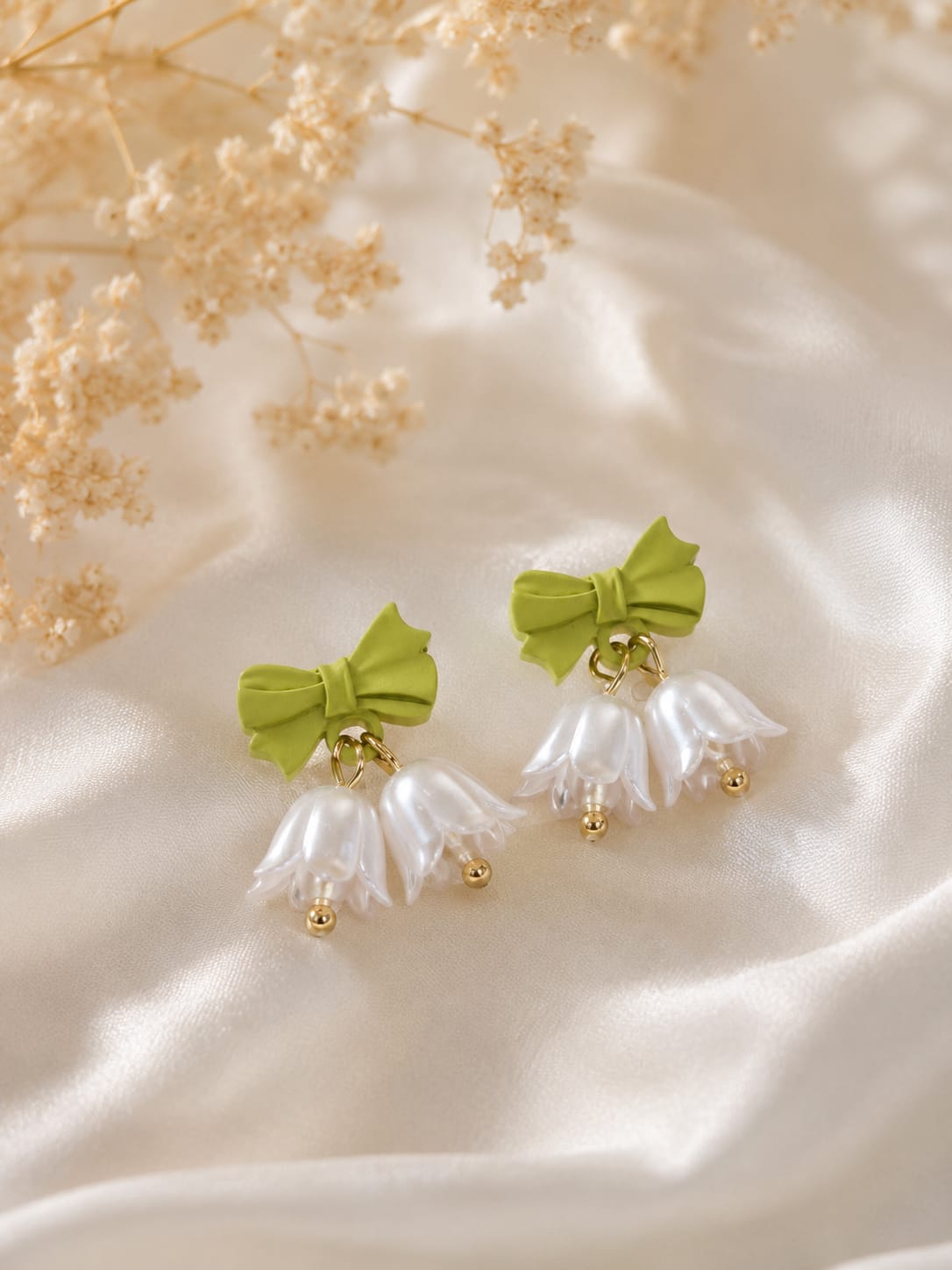 Green bow stud earrings with twin pearl lily-of-the-valley bell drops on cream satin