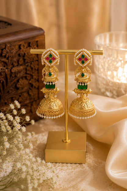 Gold-plated temple jhumka earrings with green kundan stones, a peacock dome and pearl fringe