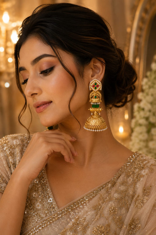 Model wearing gold-plated temple jhumka earrings with a green stone and pearl fringe